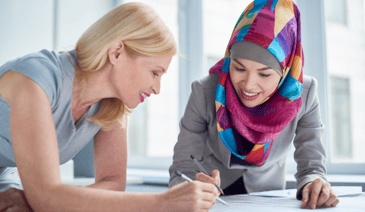 woman in colorful hijab working on papers with blonde woman