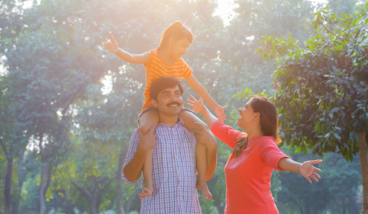 young daughter on father's shoulders while mom smiles and reaches towards her